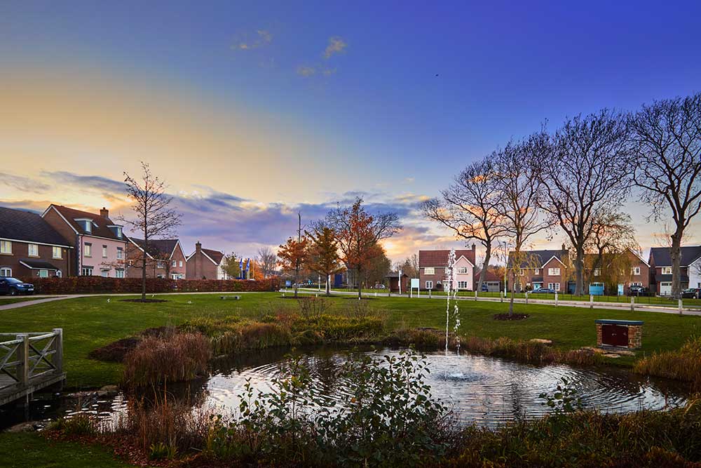 Crest Nicholson development street scene image with pond at dusk