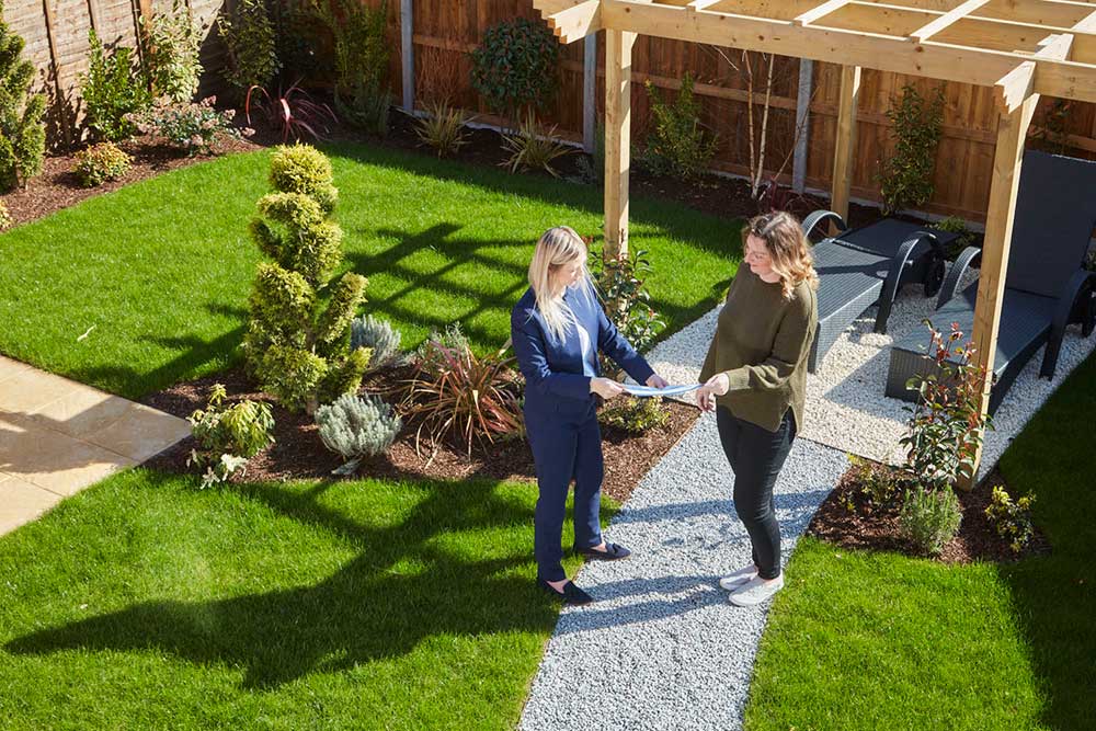 Two women standing in a garden with a pergola in the background