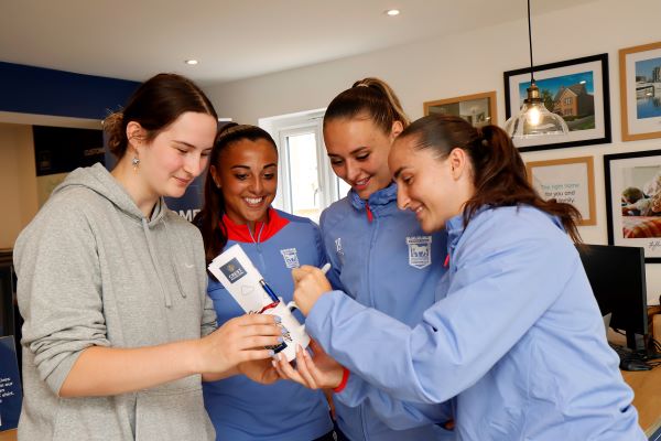 Ipswich Town Ladies FC players, Christina English and Charlotte Fleming, Ella Rutherfod and Sophie Peskett, signing a Crest Nicholson mug for a fan